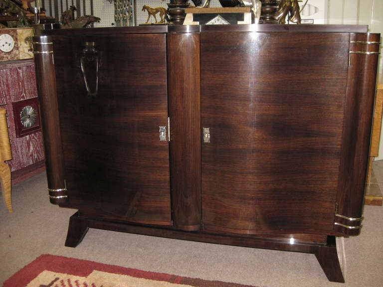Elegant French Art Deco credenza circa 1930 in palisander with sweetheart curved double door front meeting at a central slightly rounded vertical element. Nickel plated bronze escutcheons and striped accents contrast the dark wood beautifully. The