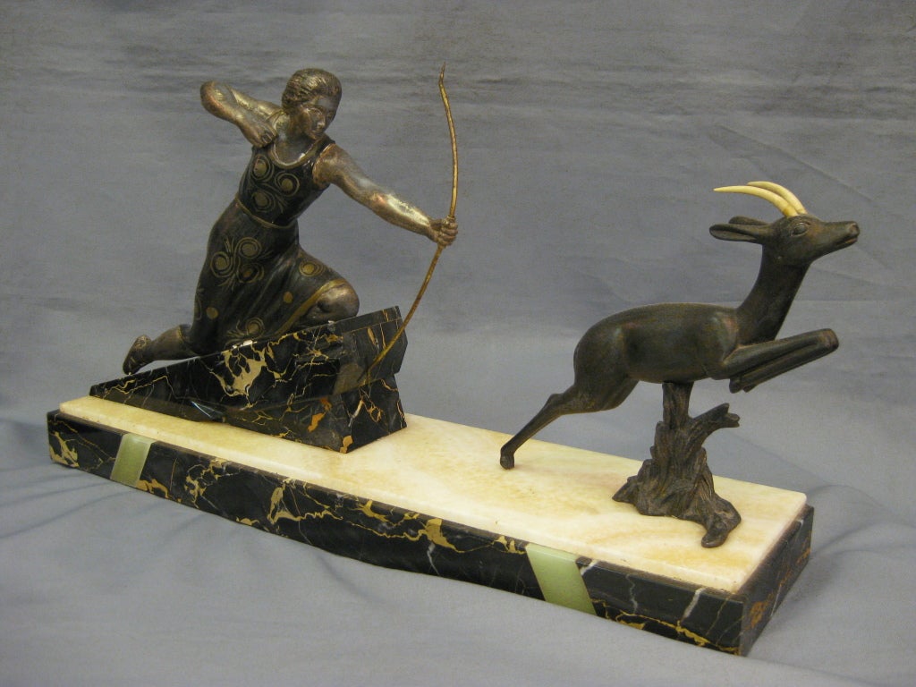 Art Deco polychrome French metal sculpture of Diana the huntress on fabulous stepped black and gold marble and inlaid two tone onyx base. The central figure is depicted as a huntress equipped with bow and leaping gazelle.
The dinanderie finish on