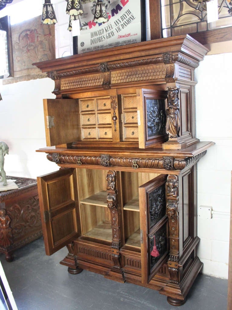 Ca. 1895 Oak storage case/hutch with stamped bronze inserts depicting a pub-scene. Heavily carved on all surfaces with figural decoration. Upper cabinets on two drawers open to reveal apothecary-style storage while the lower cabinet contains