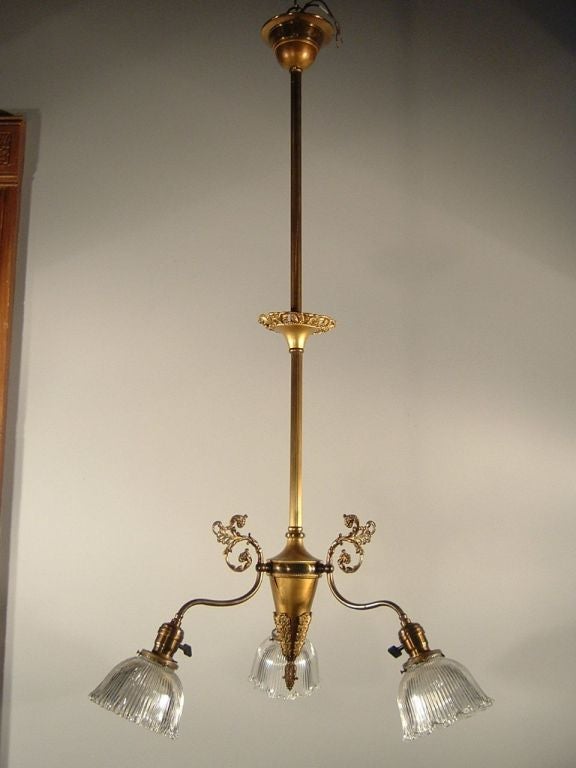 Brass Victorian three-light fixture with delicate lines and whimsical flourishes, circa. 1900. Note the integrated switches on the sockets so that each arm can be operated individually to focus light. Fitted with period re-cast holophane