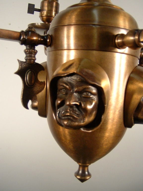 Ca. 1905 Attributed to the “Toledo Chandelier Company”, this is a unique Arts & Crafts brass combination gas/electric fixture with electrified glass tapers (originally gas). Of note are the four grimacing ‘Monk’ faces on the body and the stylized