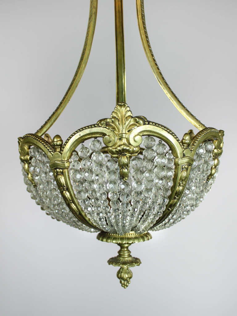 Ca. 1920 An elegant brass figural chandelier adorned with profusely-cast rams heads. Fully decorated with figural heads and foliage, the scalloped arms curl and flare to encompass a woven basket of antique crystal beads. The rippled edge of the rim