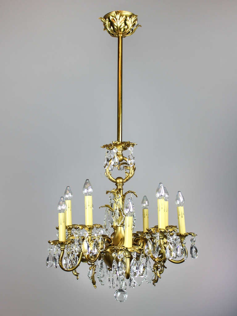 A gorgeous gold-plated brass chandelier with original finish and aged patina, circa 1910. Scrolling golden arms are decorated with cast branches of foliate and oversized luminous prisms to create a fixture that is both compact yet opulent. Converted