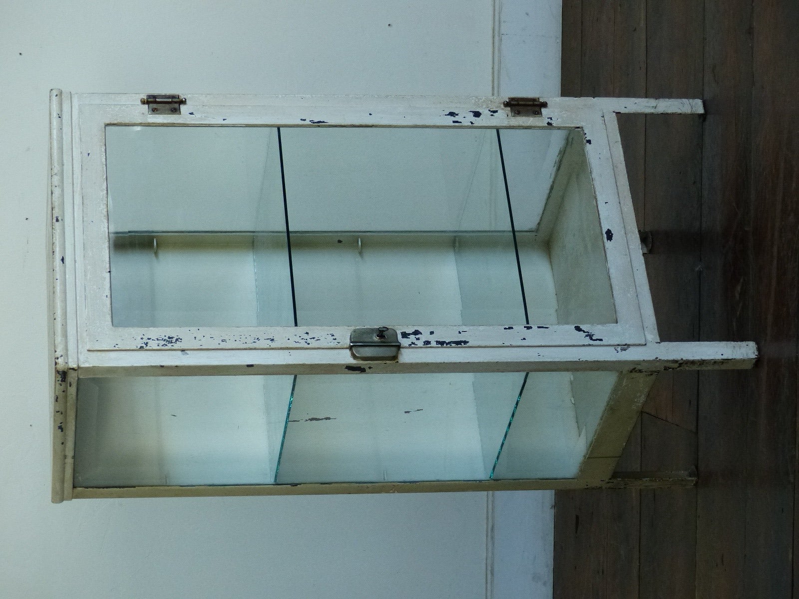 Beautiful metal three-sided glass display unit with two moveable shelves,with unusual smaller sides . Glass is beveled.
Retains old white original finish.