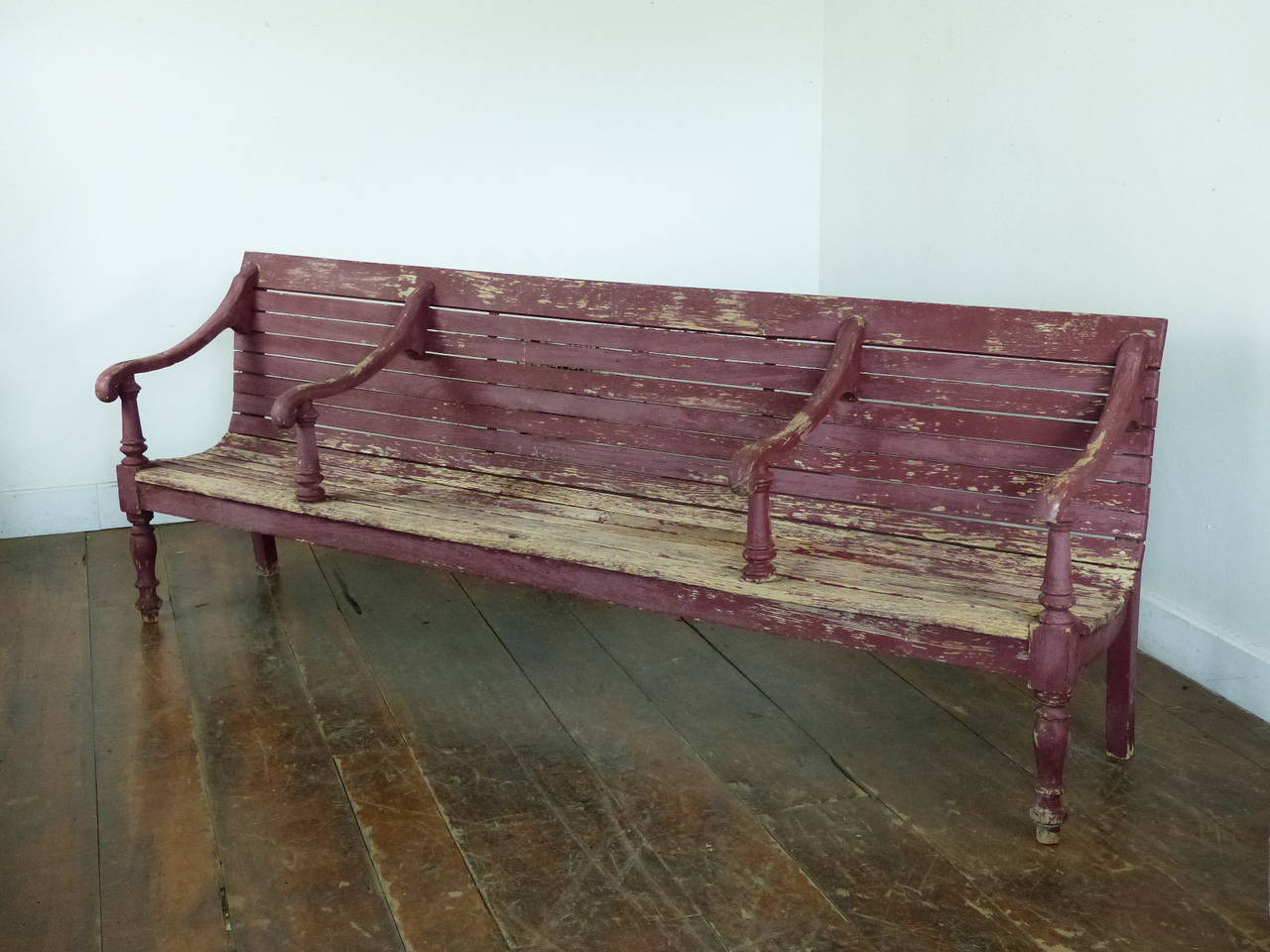Painted pine train station bench in original red surface paint. As found condition in a dry red patina. Turned legs and deter arm rest spindles add to the look