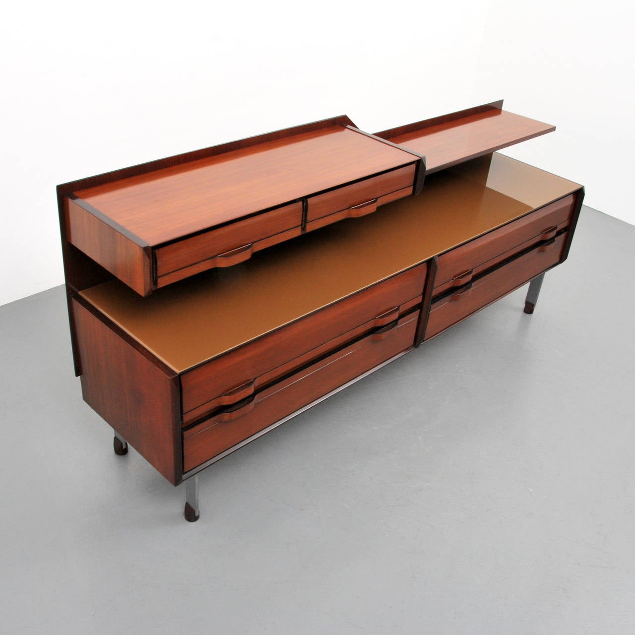 Cabinet has an upper tier with two drawers and a shelf. The lower tier has a glass top over four drawers, raised on short steel legs with wooden feet.