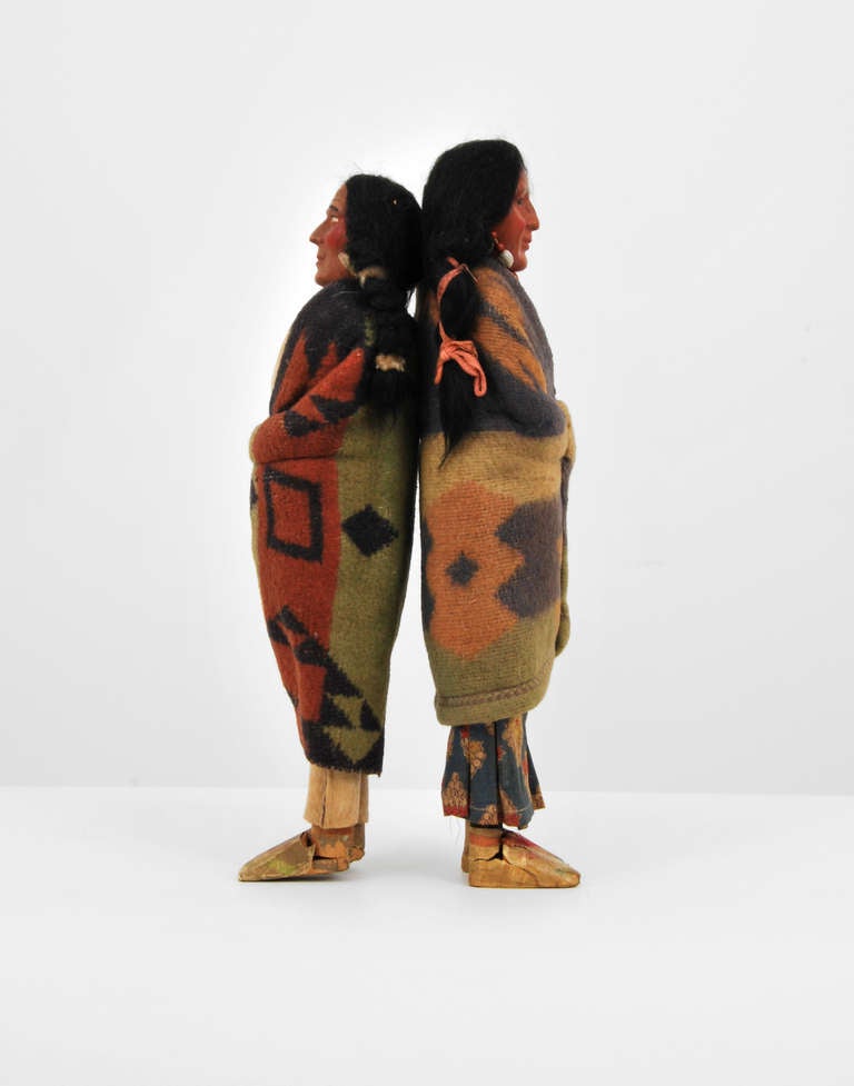 Large pair of male and female skookum dolls of braided hair, plastic faces, and wooden legs with fabric and felt clothes attributed to H.H. Tammen Co. 

