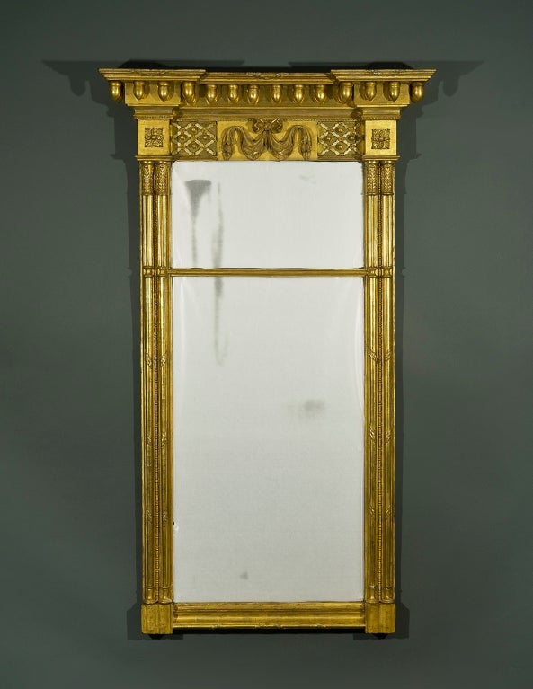 New York, circa 1815-1820.
Wood, gessoed and gilded, with mirror plate.
75 1/2 in. high, 44 1/8 in. wide (at the cornice), 8 1/2 in. deep (at the cornice).

Condition: Some restoration to carved and gessoed members and some restoration to gilding.