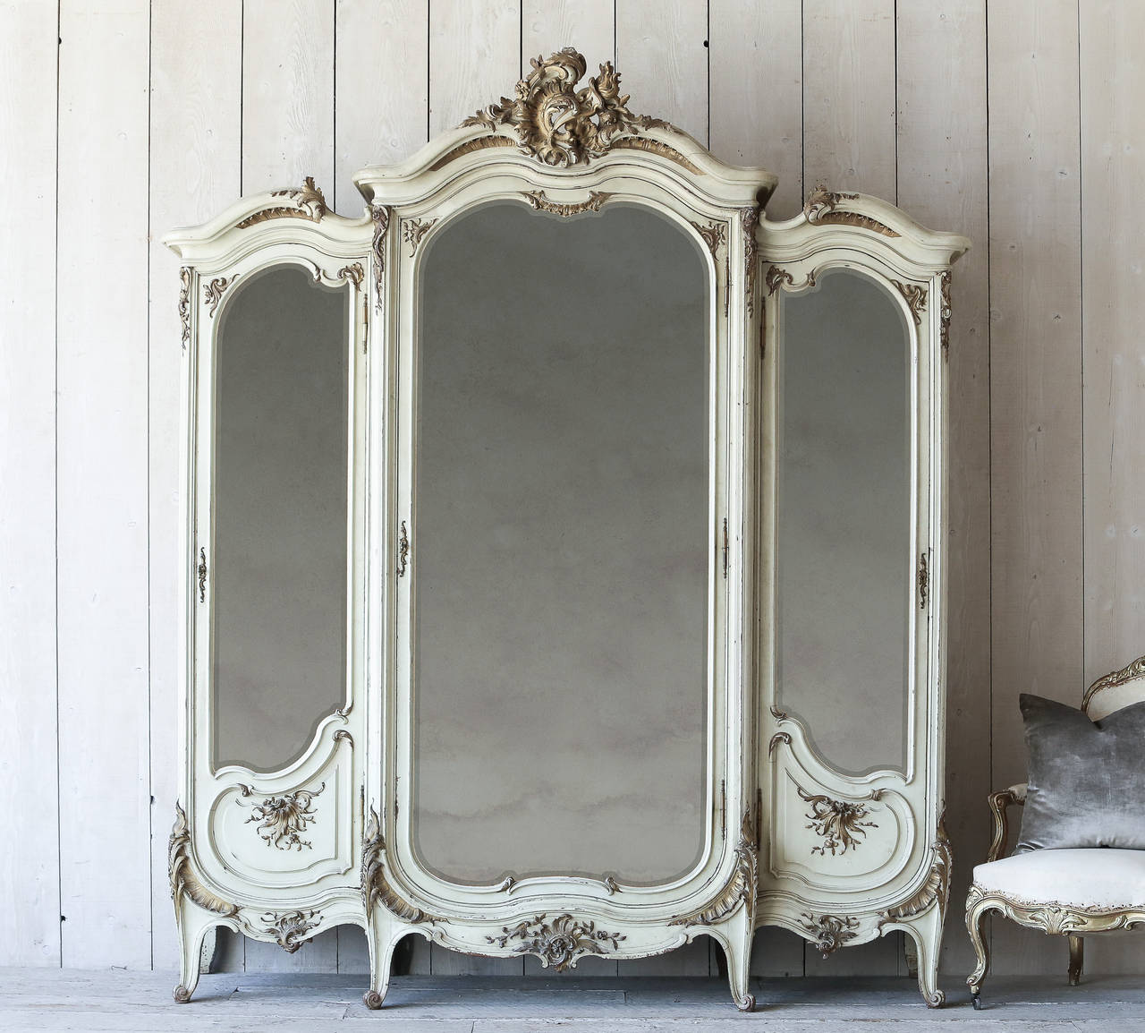 Breathtaking French antique armoire in an eggshell finish with deep gilt highlights. Flower carvings wrap this piece in grand Baroque luxury. The original beveled mirror glass is beautifully aged to perfection. Includes original keys!