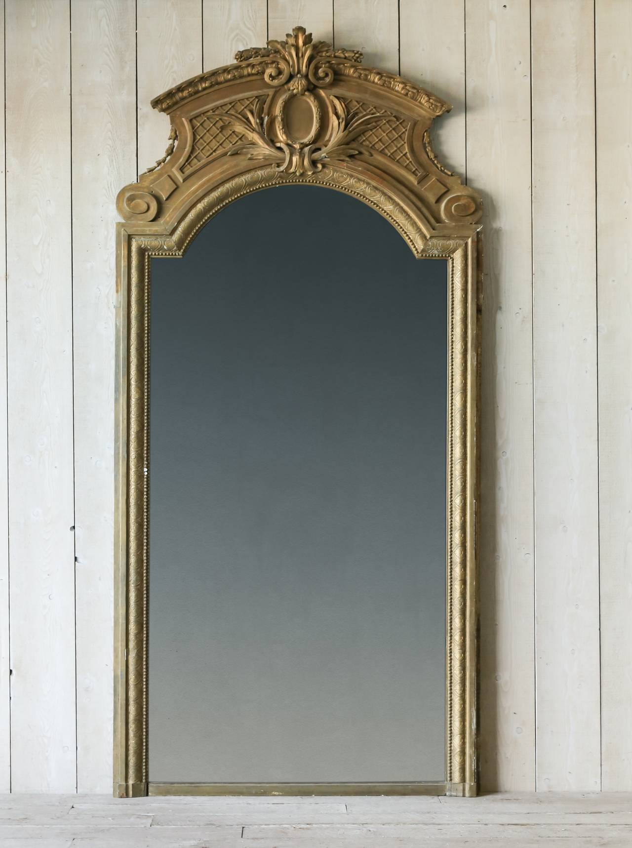 Exceptional antique ballroom mirror finished in a deep gilt, its crest adorned with a basket weave, wreath and foliage motif. The elegant, yet understated style and finish of this mirror make this piece ahead of its time. This would make a striking