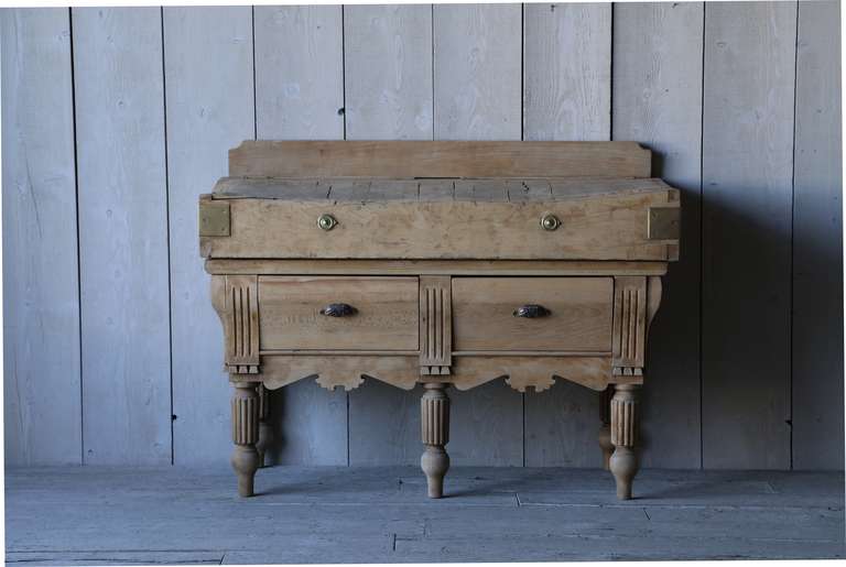 This sturdy antique butcher's block is finished in natural oak with brass toned hardware.  Bring a piece of the old world into the new with this rustic find.  This piece has stately fluted legs and a charming carved apron.  Has original slots where