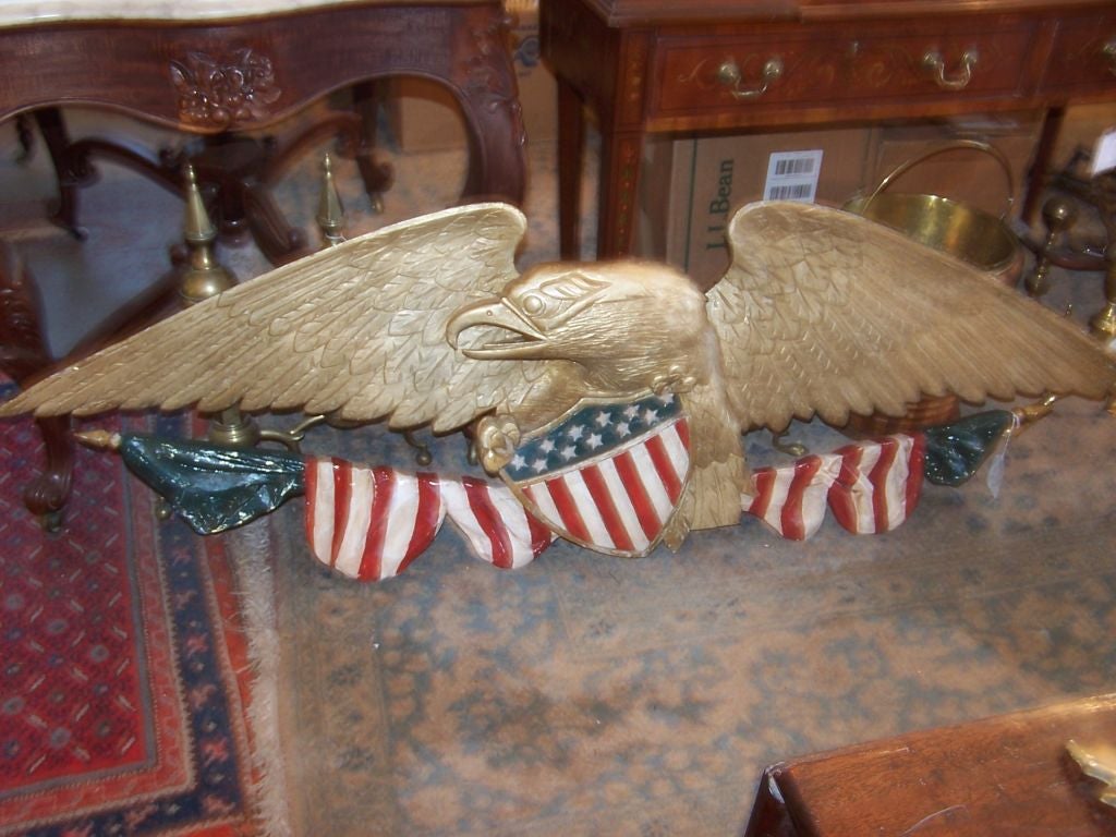 Carved, polychrome pine Eagle plaque, the eagle clutching the shield of the United States over crossed American flags.