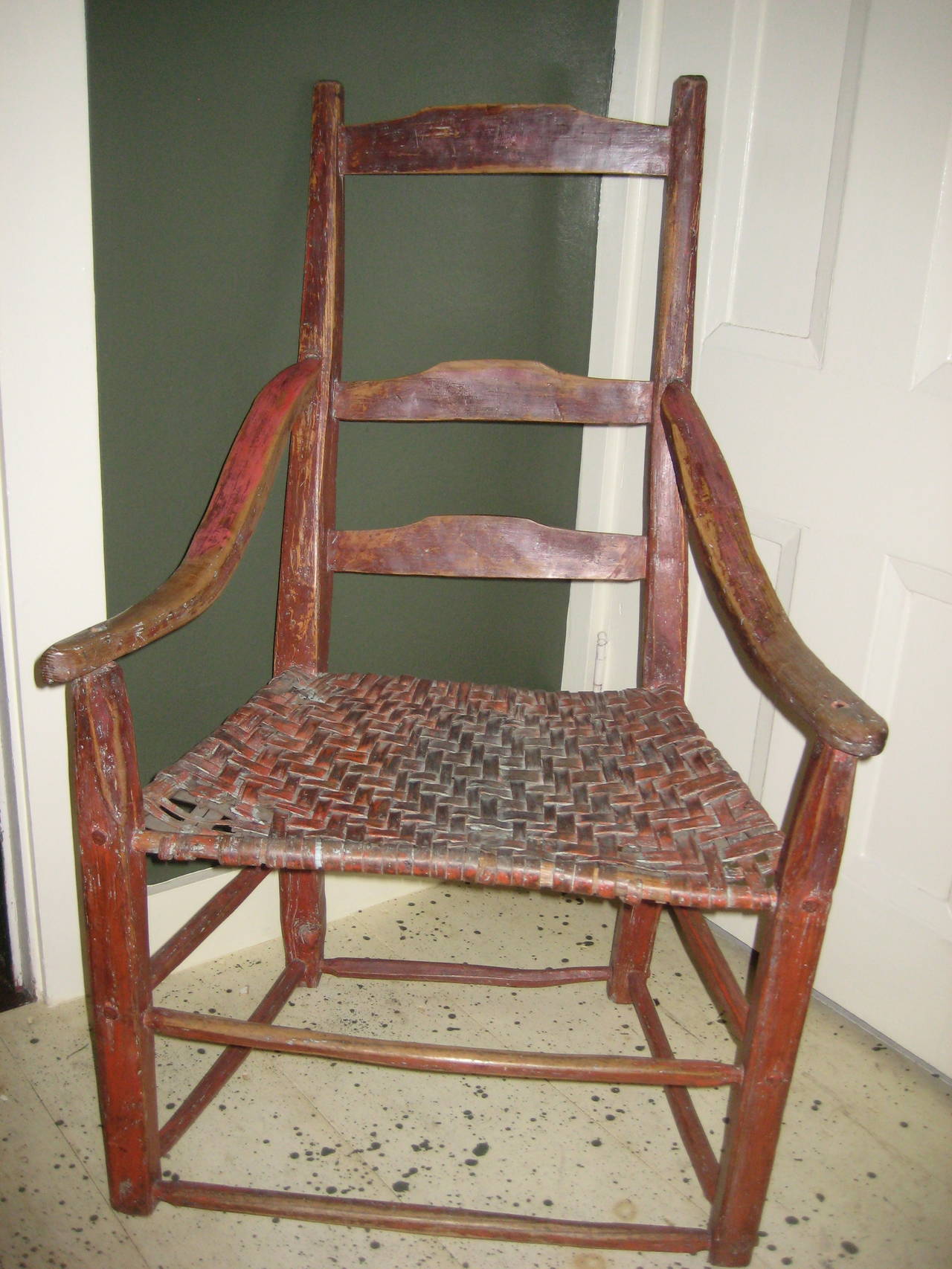 Late 18th century Canadian ladderback armchair in red paint with sloping arms and woven hickory seat.  In original, as found condition, paint on frame and seat likely original.  A true country piece with fairly rudimentary carved frame components.