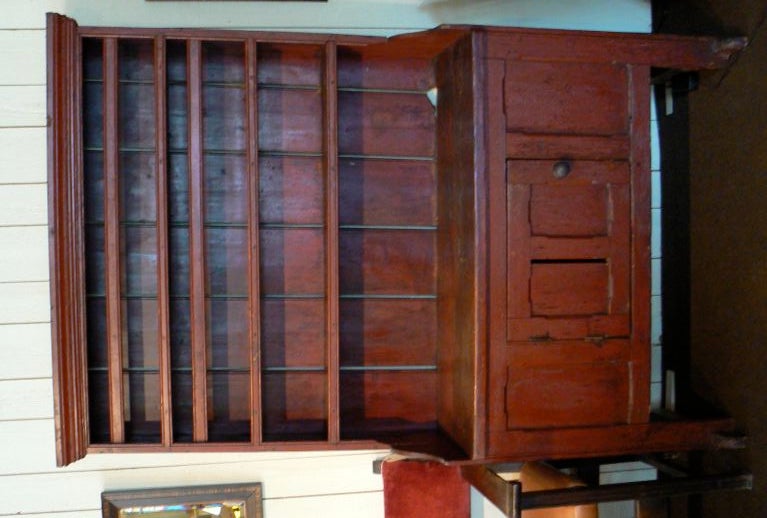 Early red stepback cupboard with single paneled cupboard door, three display shelves, and shoe foot base.  Shaped side panels and cornice molding.
