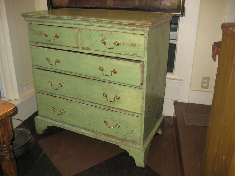 Pale green painted pine chest of drawers with bracket feet and brass handles.