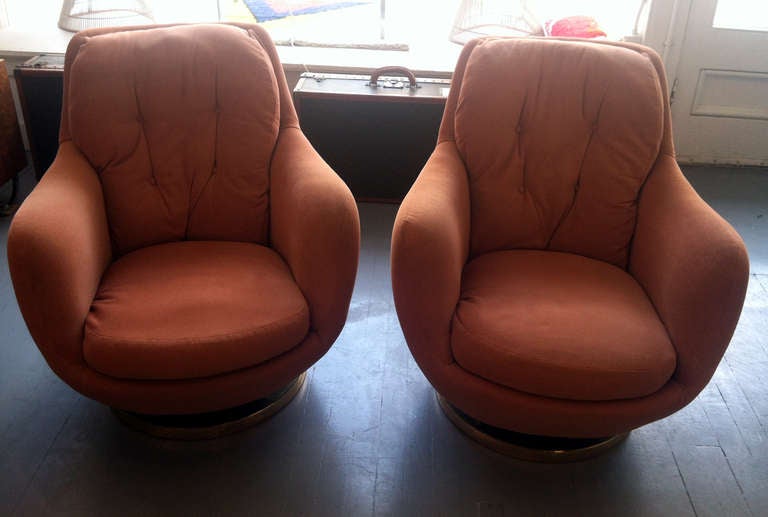 A pair of ultra chic and comfortable swivel lounge chairs designed by Milo Baughman for Thayer Coggin. Great organic form with rounded back and armrest, covered in a beautiful persimmon-color fabric with cushions and tufted details. Brass clad-round