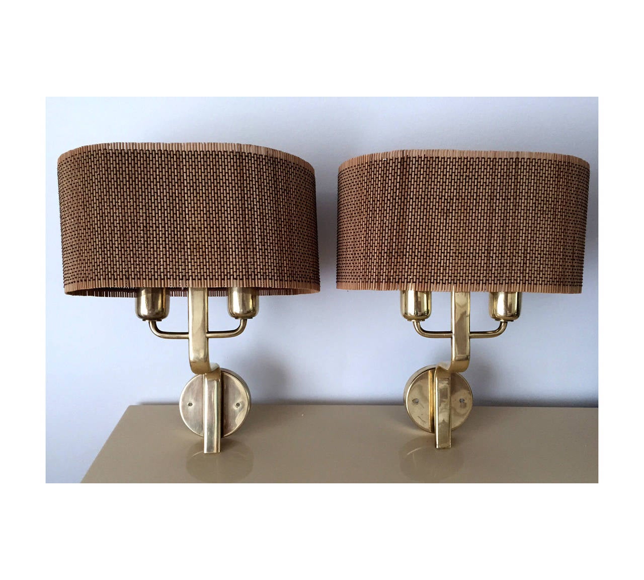 A pair of rare and early wall sconces designed by Paavo Tynell (1890-1973) for Taito Oy, circa 1940s. Made of brass with two lights and fitted with original woven rattan shades and filial plates. Ed. Taito Oy and branded on both sconces, Taito A,