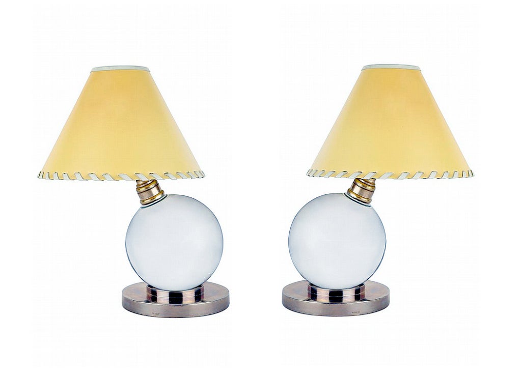 A rare pair of table lamps with cream color vellum shades by French Designer Jacques Adnet. Designed in 1930s, the petite lamps use baccarat crystal ball as the body that sits on bronze base. The design emphasized on a whimsical play between the