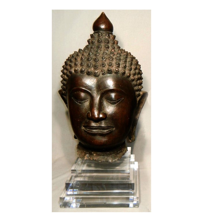 A near pair of large and imposing antique cast bronze Buddha heads, now presented beautifully on professionally mounted three-tier Lucite bases. The style of the Buddha is typical of Northern Thailand, the former Lana Kingdom. Very tranquil and