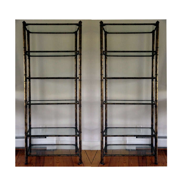 A pair of book shelves or etageres in Hollywood Regency style. Constructed with patinated metal frame in faux bamboo forms and completed with removable glass shelves. Each features five shelving spaces with height of 13, 13, 13, 16 and 10 inch each,