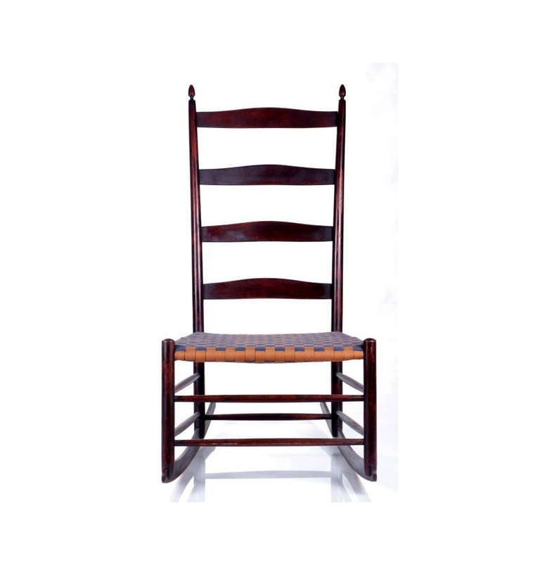 A Shaker rocker chair constructed with stained Maple. It features a ladder back, turned filial and webbed seat. Branded #6. Period piece from early 20th Century. Likely made in Mount Lebanon Shaker Community in New York. Beautiful form with