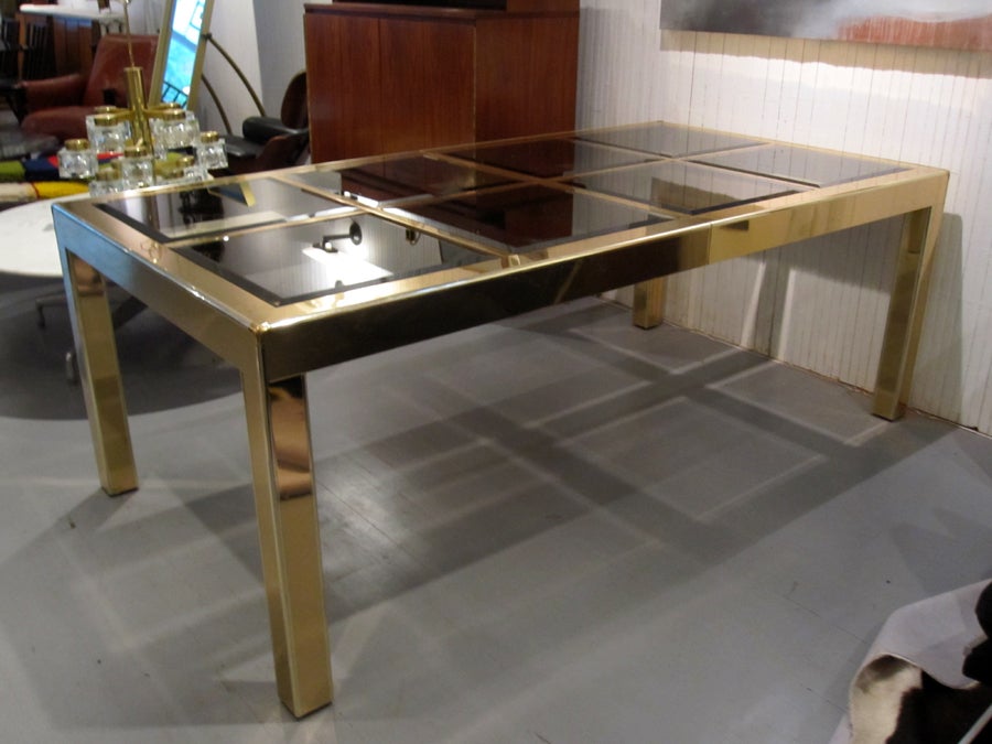 A large dining table made of brass, wood and glass by Mastercraft. Simple grid construction features bevelled smoked color glass panels. Brass veneer with thin chrome trims and corner details. It measures 81 inches without leaves. With two 20 inch