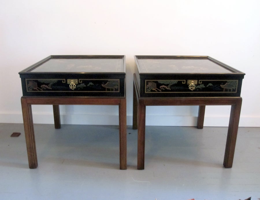 A pair of tables with drawer on stands that can function as night stand or side table. Made by Drexel Heritage in an oriental Chinoiserie taste. It features squared mahogany legs supporting a black lacquered drawer with painted decoration on the