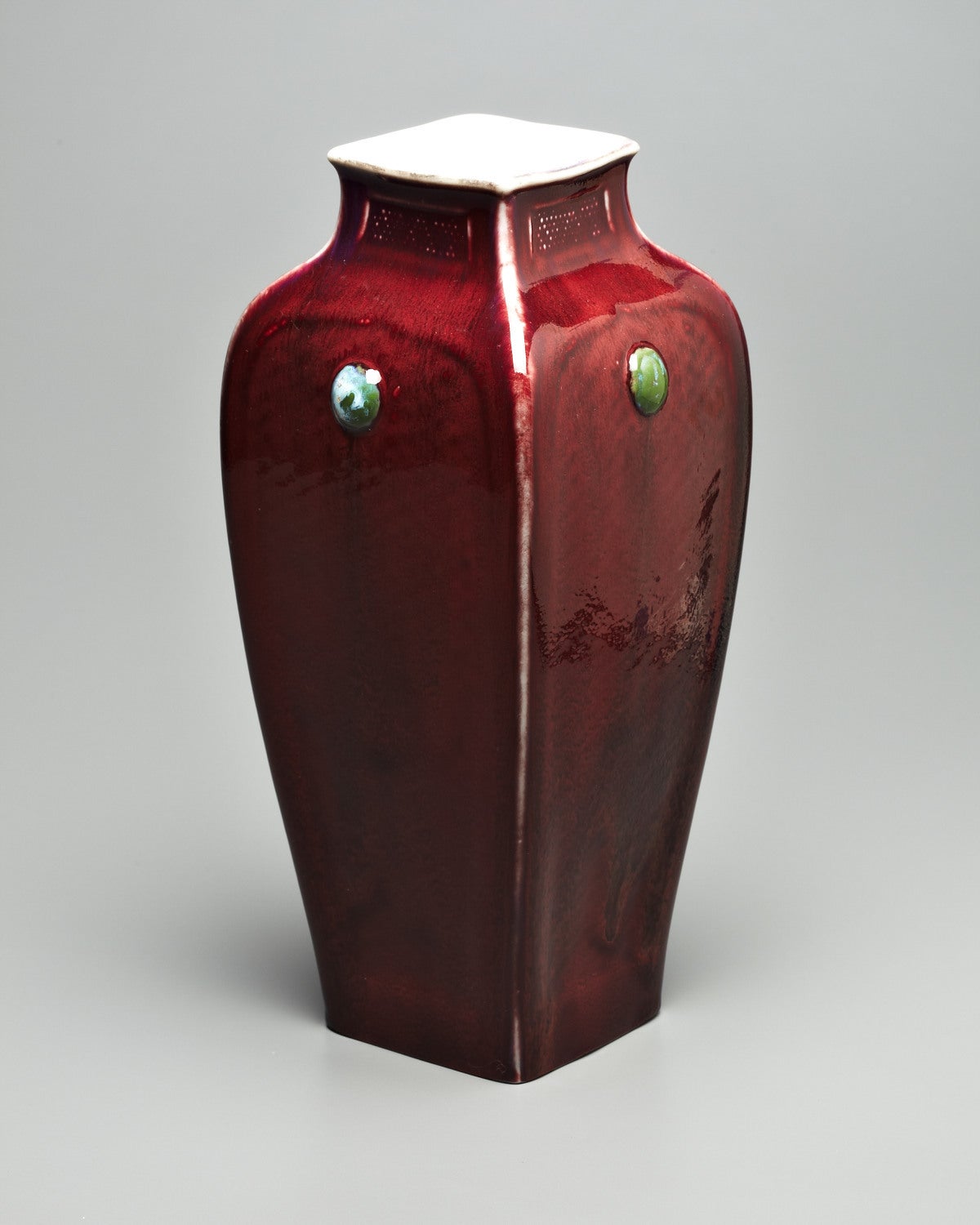 This stunning four-sided vase is covered in a rich sang-de-boeuf glaze, which thins at the edges, exposing the vivid white porcelain. Jade colored medallions with an alluring marbleized effect encircle the form at shoulder height. Marks: Painted T