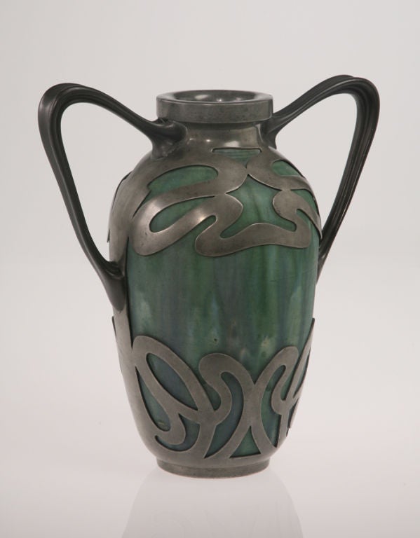 A stoneware vase with a mottled green glaze, set in a metal mount that also forms two handles, this is a powerful example of the whiplash line that was so vital to Art Nouveau design. Alexandre Bigot (1862-1927), a physics and chemistry teacher who