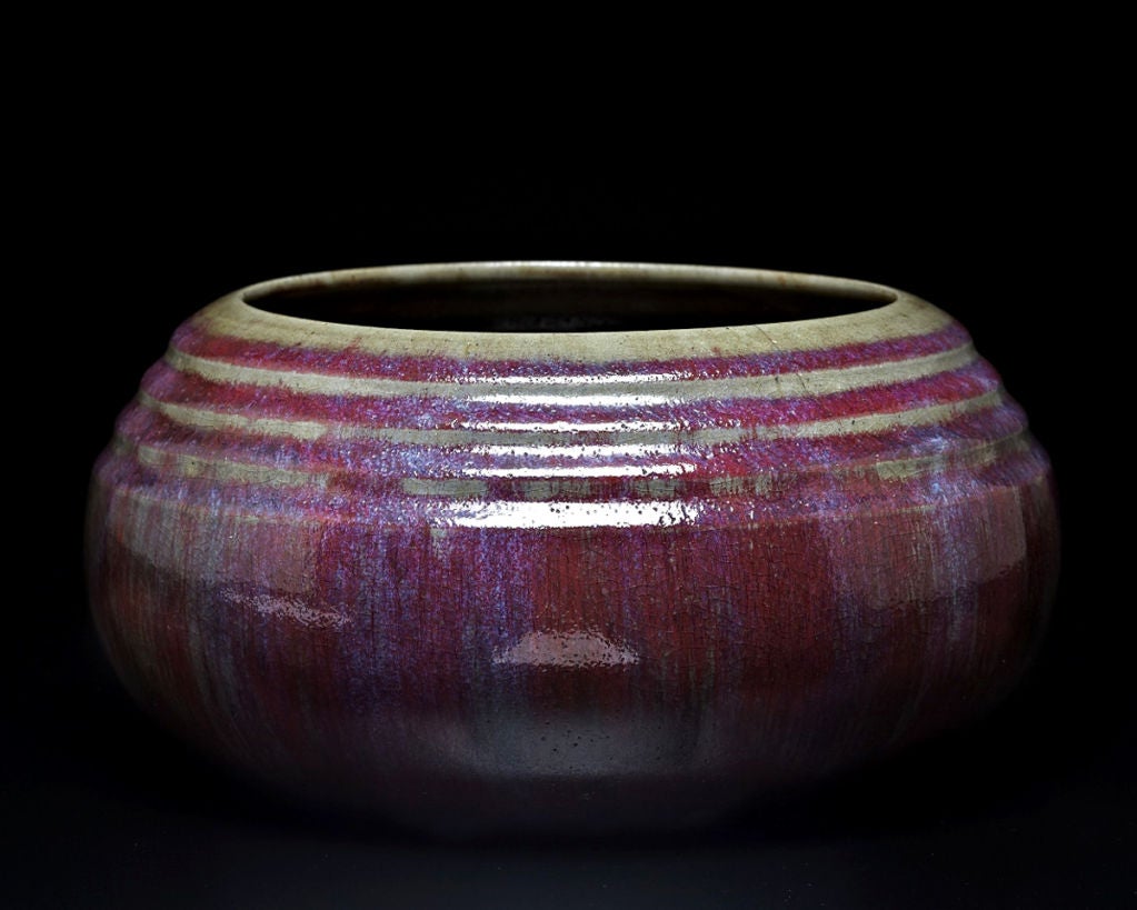 This squat stoneware bowl features a vibrant glaze decoration, streaked with rich shades of red, purple, magenta and blue. A series of ridges and furrows encircling the rim add texture to the form, while causing the underglaze to remain exposed in