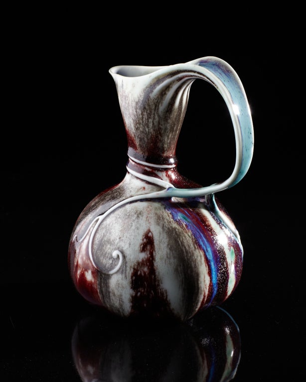 A sinuous tendril flows seamlessly from the rim of this gourd-shaped ewer, gracefully curving downward and wrapping around the neck, the swirling tips of the vine gently adhering to the bulbous body. Decorated in a fantastic sang-de-boeuf glaze with
