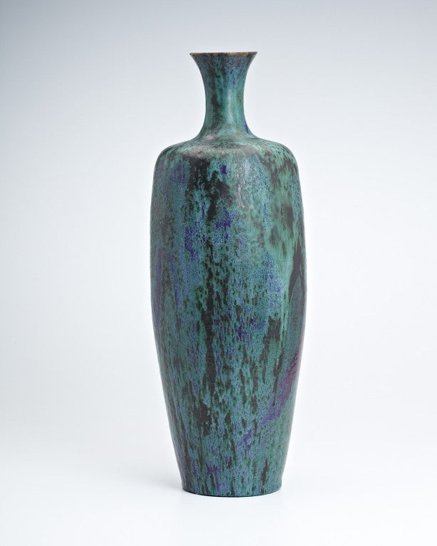 Reminiscent of an ancient patinated copper vessel, this tall graceful form, high-shouldered, with a flaring mouth is decorated in an exquisite flambé glaze in shades of green. Flashes of sang-de-boeuf and turquoise shine through, as the glaze drips