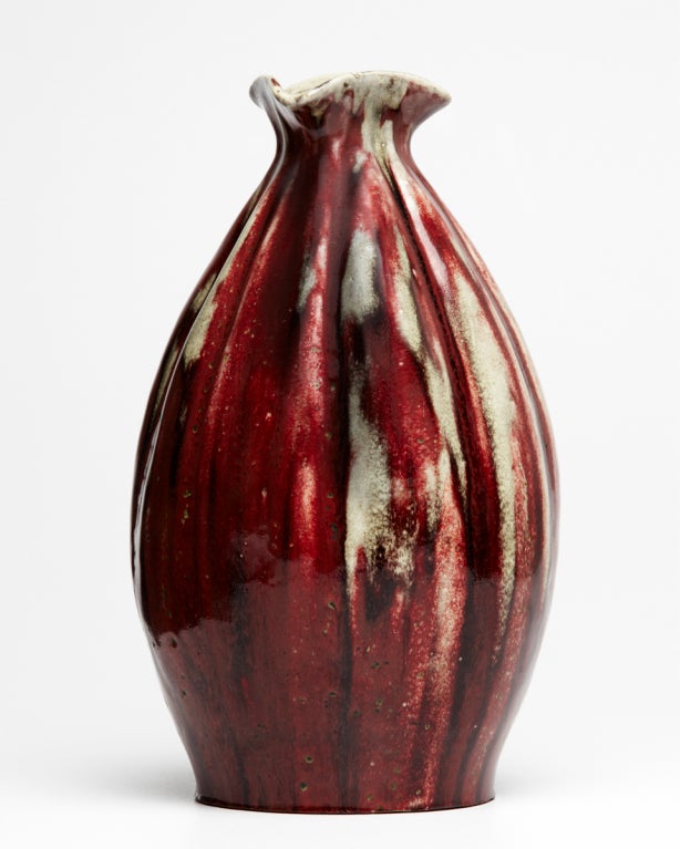 The vertical ribs of this fantastic gourd form vase add a rich texture, while providing avenues for the shedding and pooling of the superb sang de boeuf glaze. The swelling form tapers at neck, then flares out into a distinctive tri-corner shaped