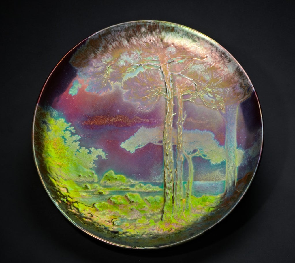 This charger features a peaceful lake scene with a vantage from the shore. The psychedelic quality of the iridescence is amplified by the realistic subject matter. This scene is one that Massier revisited in several other of his works.