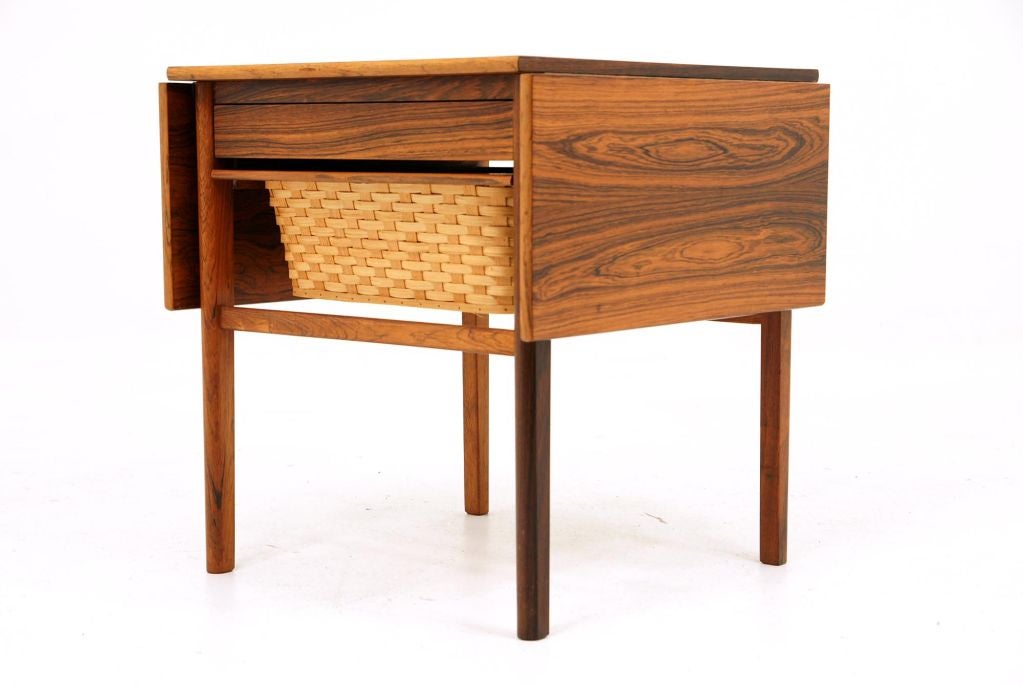 Rosewood Danish sewing table with spool drawer and pull out knitting basket. Two small drop leaves raise and are held up by slide out bars from underneath. One small spot on the top as seen. Original condition.