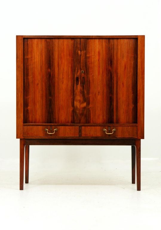 Rosewood bar or cocktail cabinet from Denmark. Two tambour or sliding doors above to drawers. Small shelving, mirror and contoured shelving within. Condition superb and original keys included.