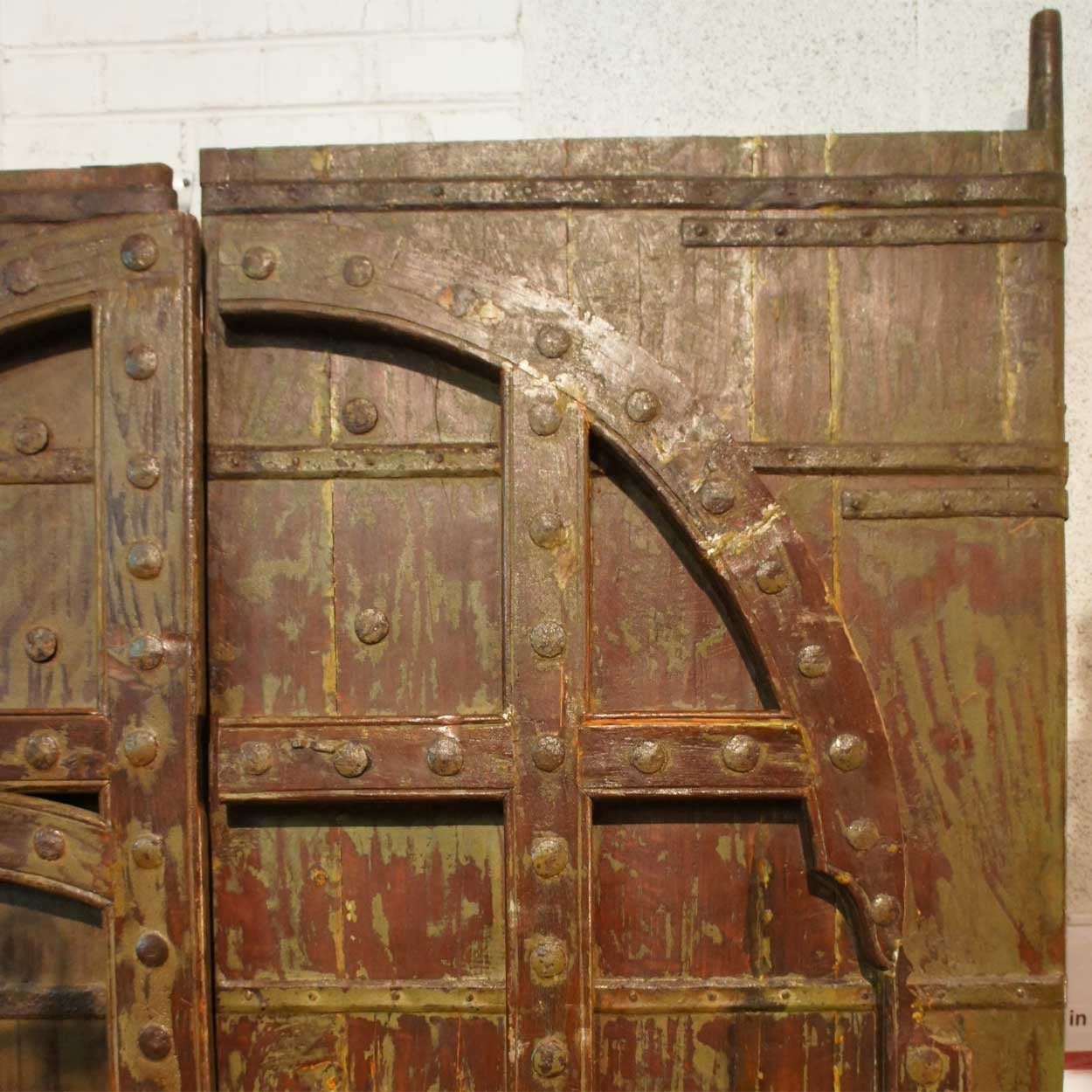 This massive, antique Indian double-door gate features an inset pedestrian door for ease of entry. Built for strength, they are crafted of thick teak with iron strapping and hand-forged nails. It is decorated with traditional thick, arched moldings