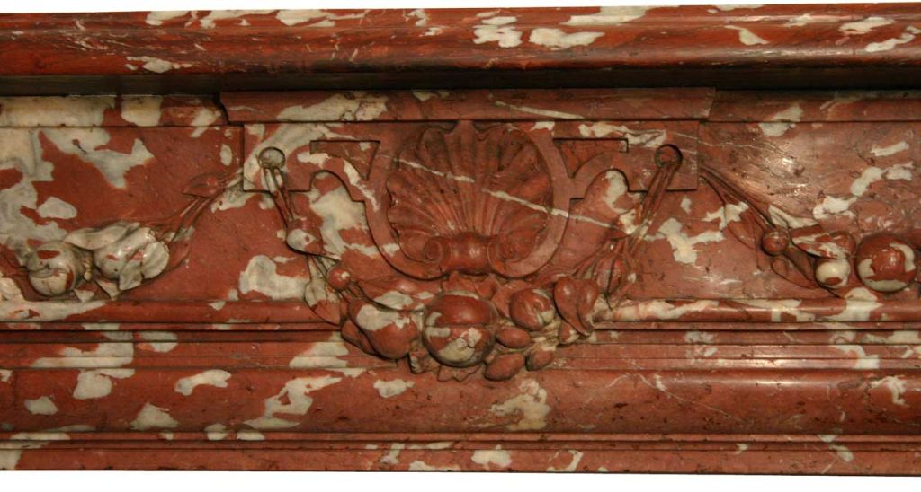 Employing Louis XV and XVI decoration, this beautiful chimney was hand fashioned in brick red, Languedoc marble, with the typical prominent, white mottling; the entablature featuring a mantel overhanging the decorative frieze, carved with a central