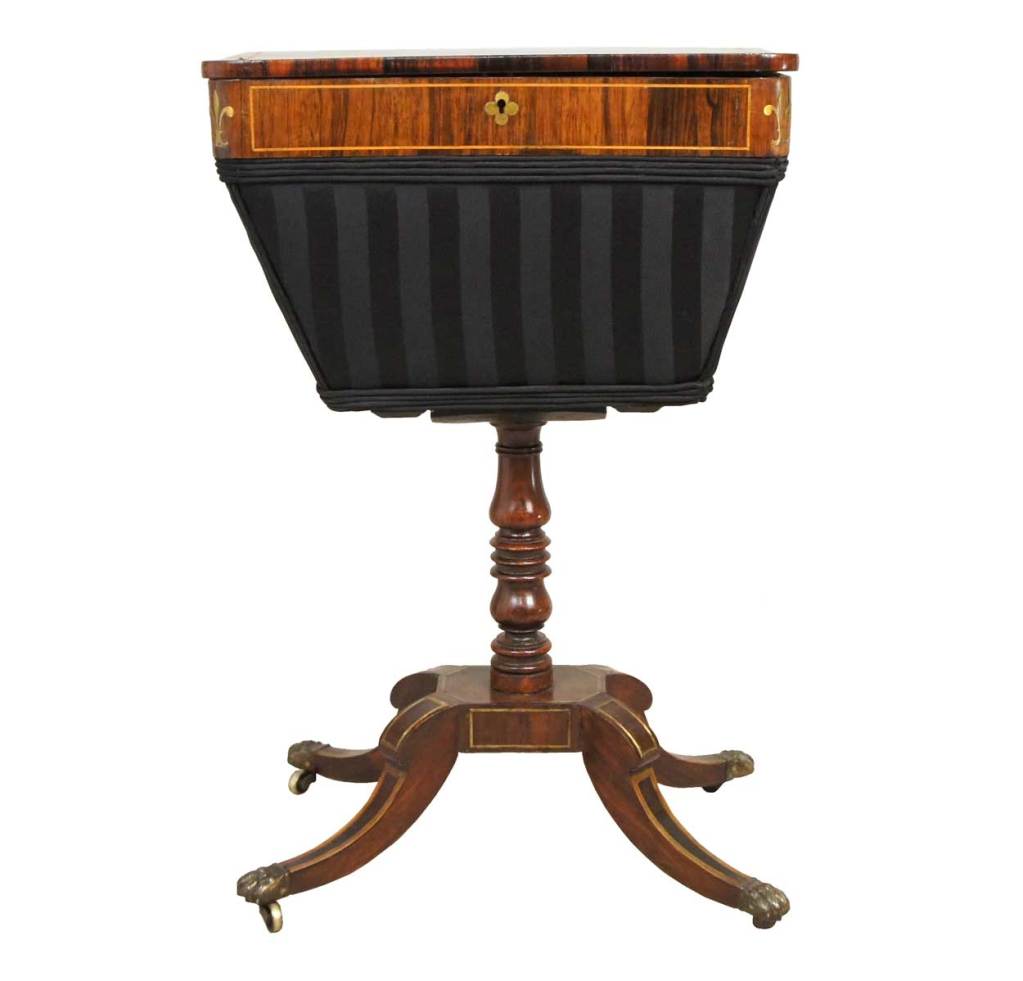 Crafted of well figured rosewood, the box displays a rounded corner, hinged lid that opens to a fitted interior for sewing accessories. The exterior is inlaid with satinwood fleurs-de-lys and brass stringing, above a tapering newly upholstered,
