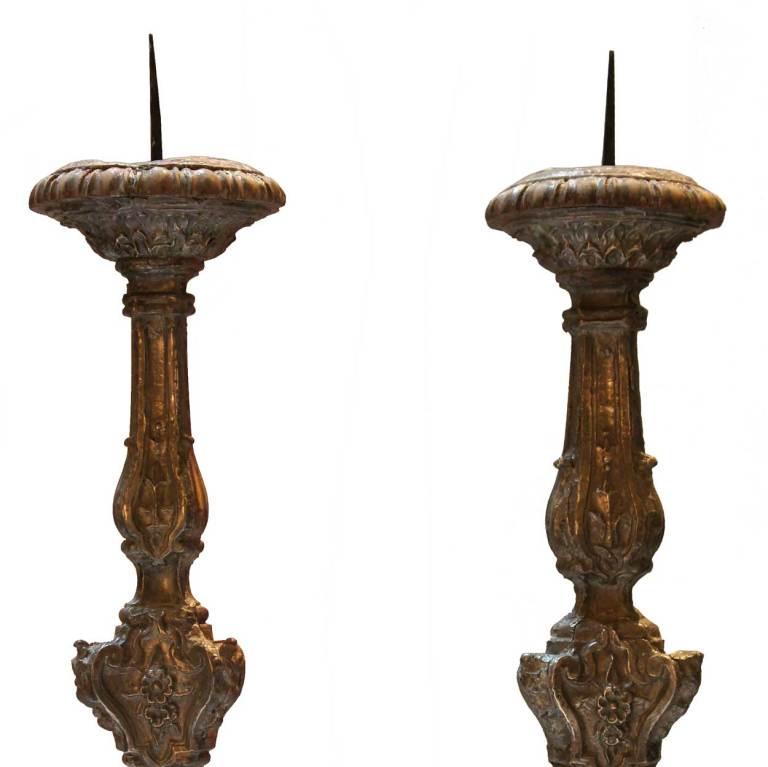This rococo pair of pricket sticks was intended for altar use. The hand carved teak base, is covered with silver repoussé with leaf designs on the broad drip pan, a floral design below the waist on the stem and shell and leaves on the scrolled base.