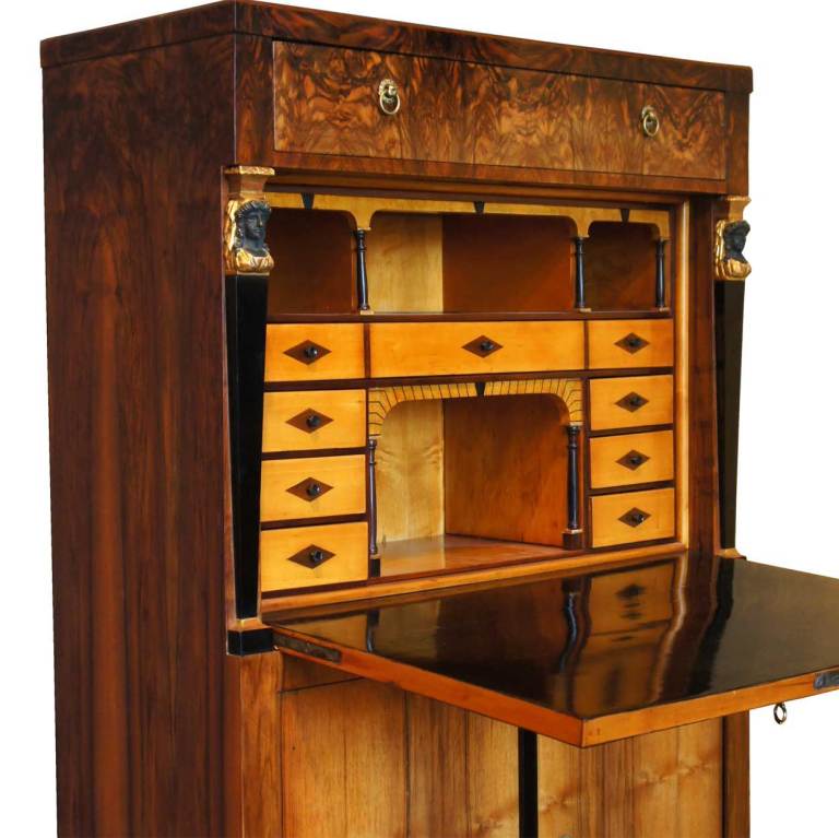 This tall cabinet is fitted with a long drawer above architectural pilasters flanking a fall-front writing surface, opening to reveal an arrangement of small drawers and pigeon-holes; the base with a pair of double cabinet doors on squared tapering
