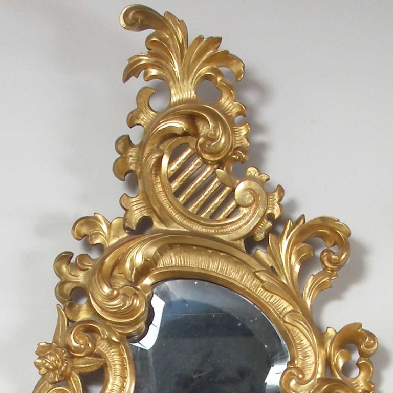 Each shaped, asymmetric beveled mirror is framed with gilt, pierced rocaille ornament, foliate, flowers and C-scroll decoration and surmounted by predominant foliate C-shaped auricular crests. They each also feature a pair of staggered display