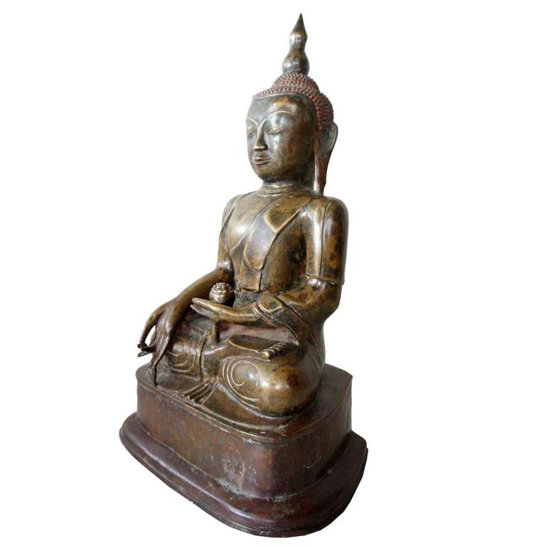 This early, antique buddha sits cross legged in a traditional dhyanasana pose on a simple plinth that is flat on the back side. The serene face displays a slight smile, with the hair in an oval topknot (ushnisha) rising to a tall lotus bud finial.