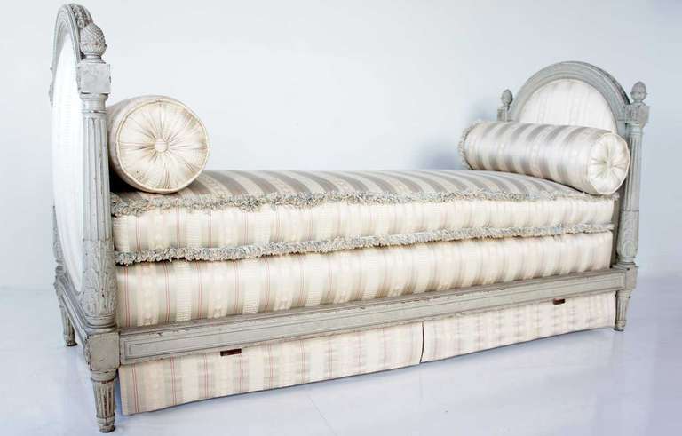 This elegant day bed is crafted in the French style of 18th century. It features an oval upholstered head and foot boards in a subtle cream and red stripe fabric. The frame is classically carved with carved pineapple finials and foliate details. It