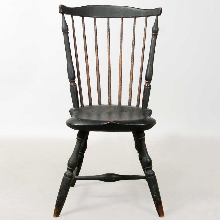 This fan-back chair has a bowed, shaped crest rail above seven spindles and turned stiles, with a saddle seat raised on splayed turned legs with a swelled H-stretcher. Retains an old and well-worn paint history of black over green. Provenance: from