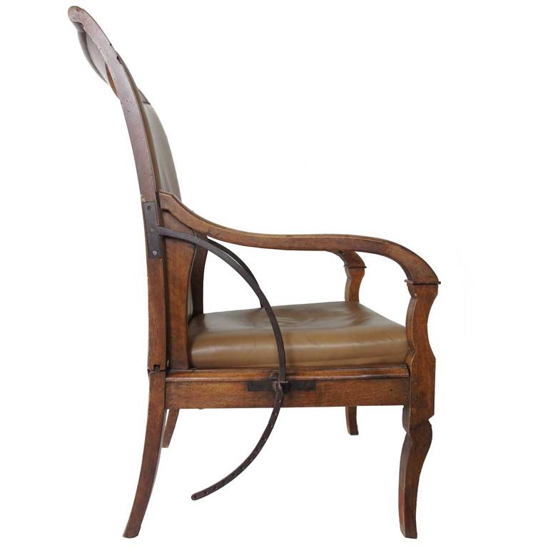 A  forerunner of the recliner, this antique French open armchair or fauteuil displays a tall, curved back that reclines on an adjustable, forged iron mechanism. It is upholstered on the back and seat with tan leather and edged with nail heads, with