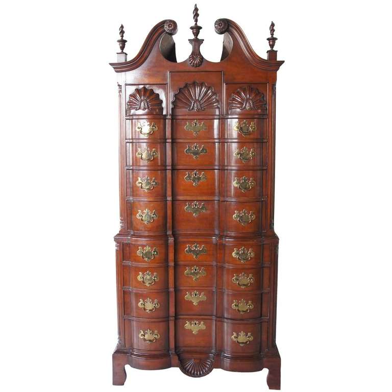 Constructed in the early 20th century, this is a bench made, handcrafted reproduction of an 18th century chest on chest. It features a bonnet top with three flaming urn finials. The two-part block front case displays convex and concave shell