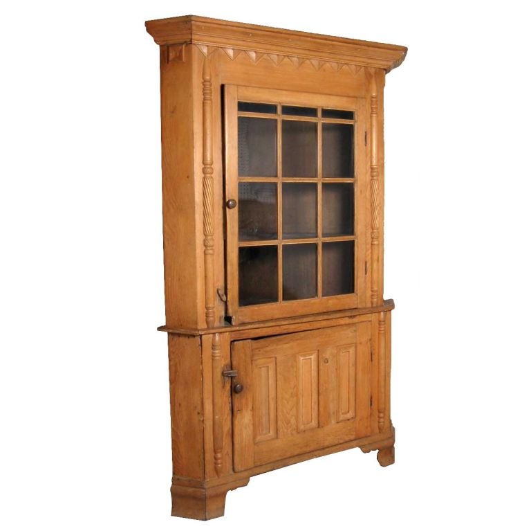 From Reading, Pennsylvania, this canted corner cupboard has a molded cornice above a distinctive triangle pattern frieze. The top section has a single glazed door opening to a shelved interior and flanked by ball and spiral turned pilasters. The