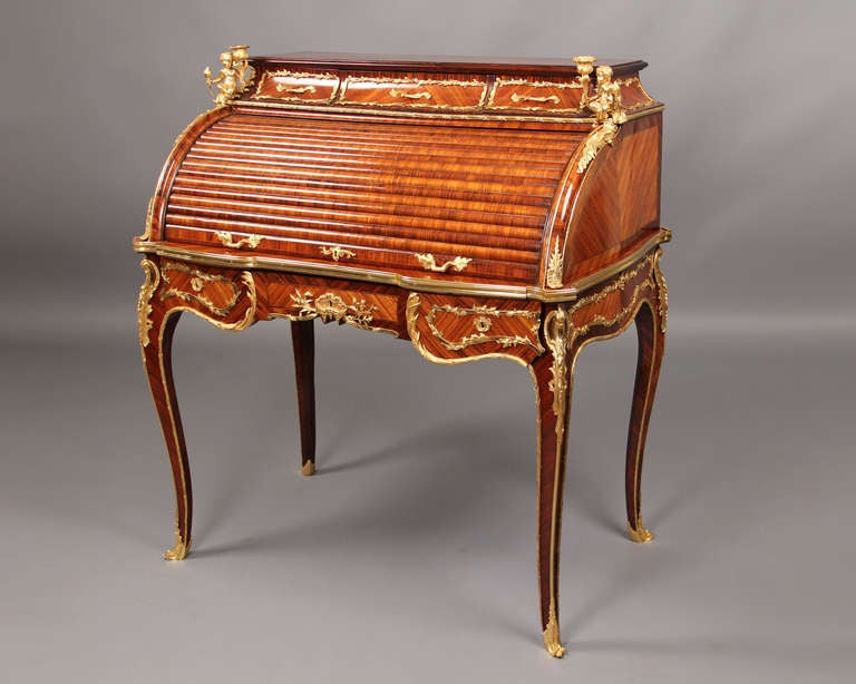 A Late 19th Century Louis XV Style Gilt Bronze Mounted Rolltop Desk

Rectangular top above three frieze drawers, the interior writing surface leather-lined ,fitted with three alcoves with two drawers. the angles headed by putti holding candelabra,