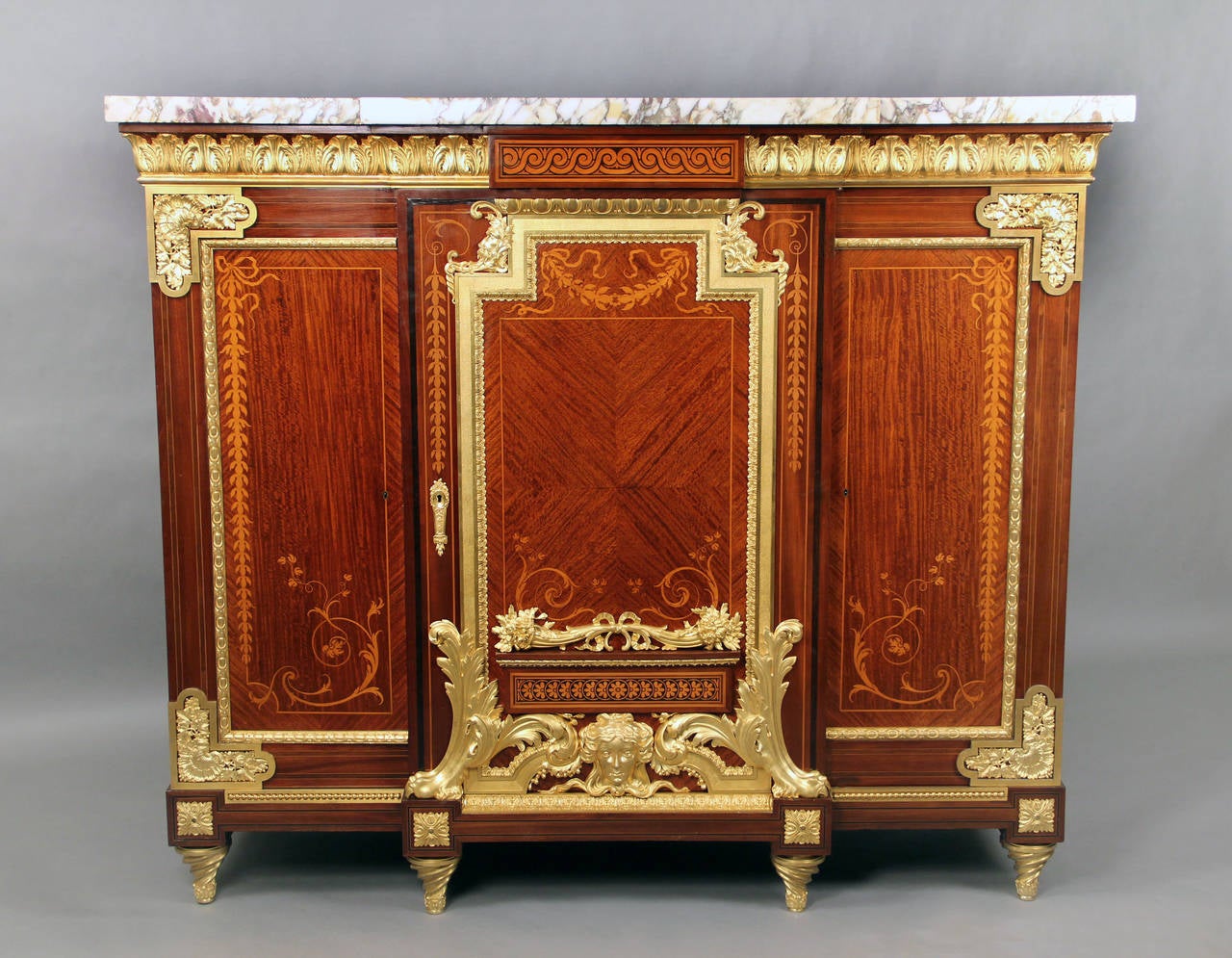 A rare and palatial late 19th century gilt bronze-mounted Louis XVI style marquetry and parquetry cabinet.

A heavy marble-top above a bronze frieze with three paneled doors decorated with inlaid floral marquetry designs. The center door with gilt